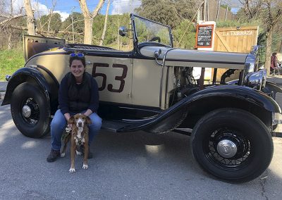 Mujer posando con un perro junto a un coche antiguo